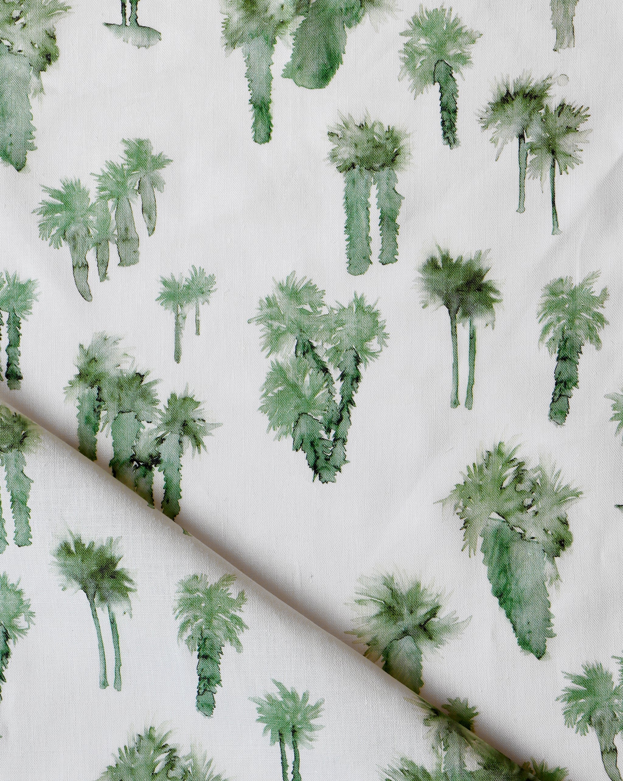 Draped fabric yardage in a painterly palm tree print in shades of green on a white field.