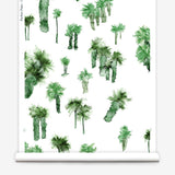 Partially unrolled wallpaper yardage in a playful palm tree print in shades of green on a white field.