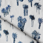 Draped fabric yardage in a painterly palm tree print in shades of navy on a white field.