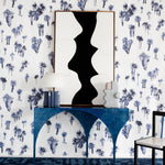 A modernist end table with art stands in front of a wall papered in a playful palm tree print in navy, gray and white.