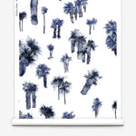 Partially unrolled wallpaper yardage in a playful palm tree print in shades of navy and gray on a white field.