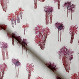 Draped fabric yardage in a painterly palm tree print in shades of red and purple on a white field.