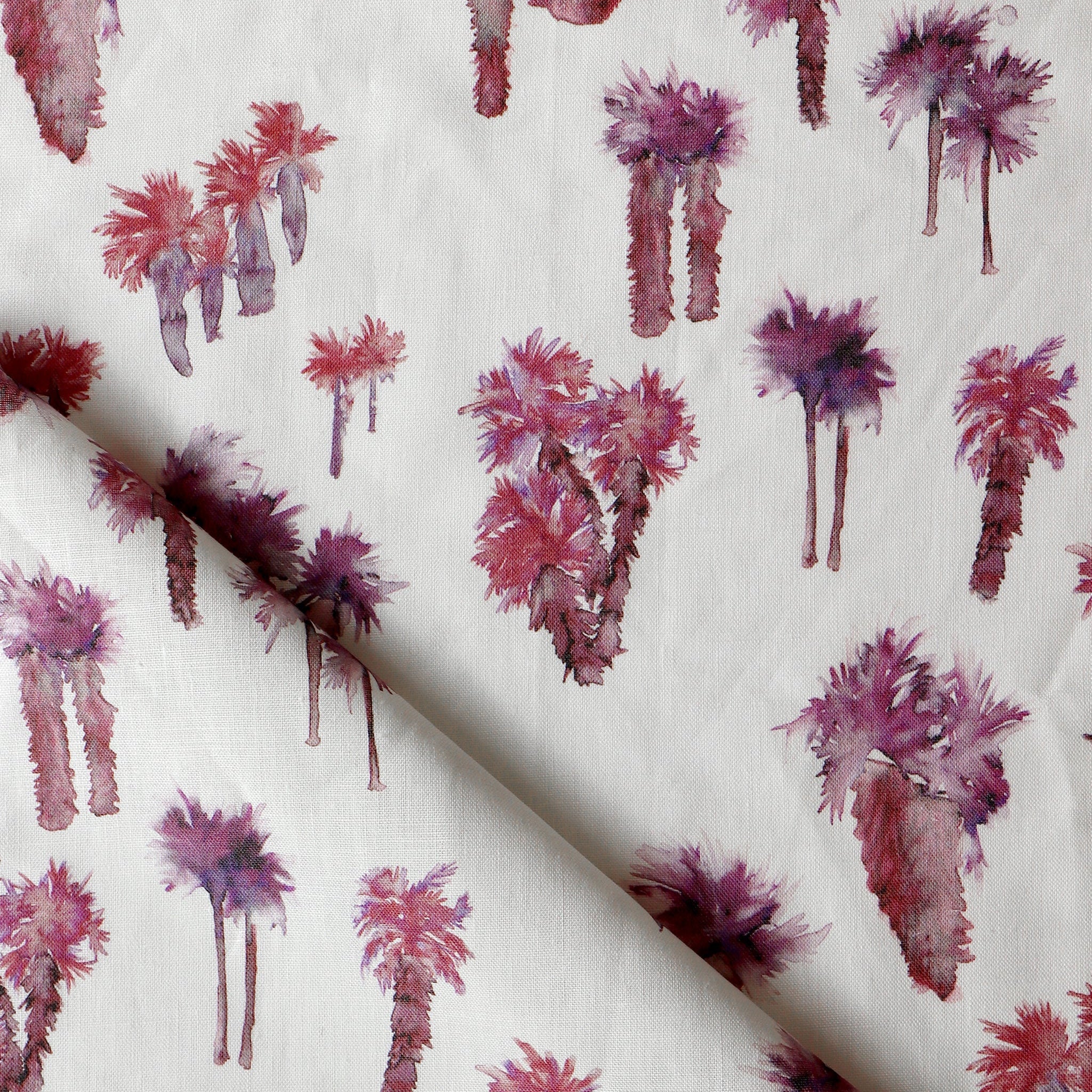 Draped fabric yardage in a painterly palm tree print in shades of red and purple on a white field.