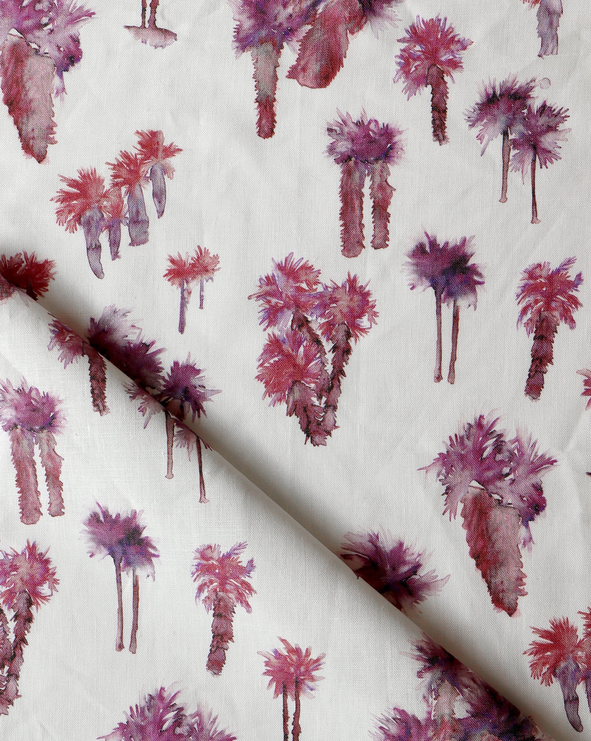 Draped fabric yardage in a painterly palm tree print in shades of red and purple on a white field.