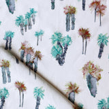 Draped fabric yardage in a painterly palm tree print in shades of brown, gray and turquoise on a white field.