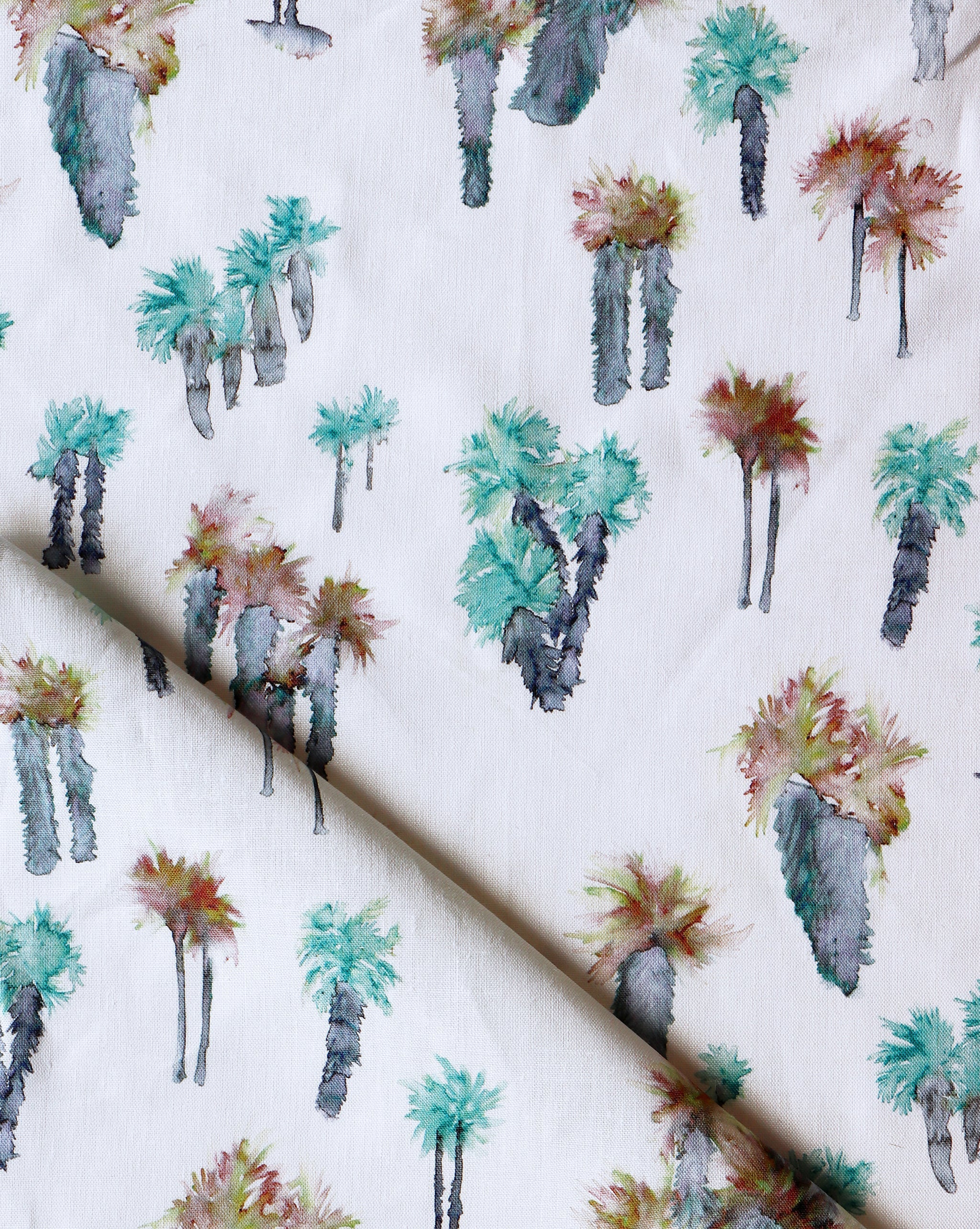 Draped fabric yardage in a painterly palm tree print in shades of brown, gray and turquoise on a white field.