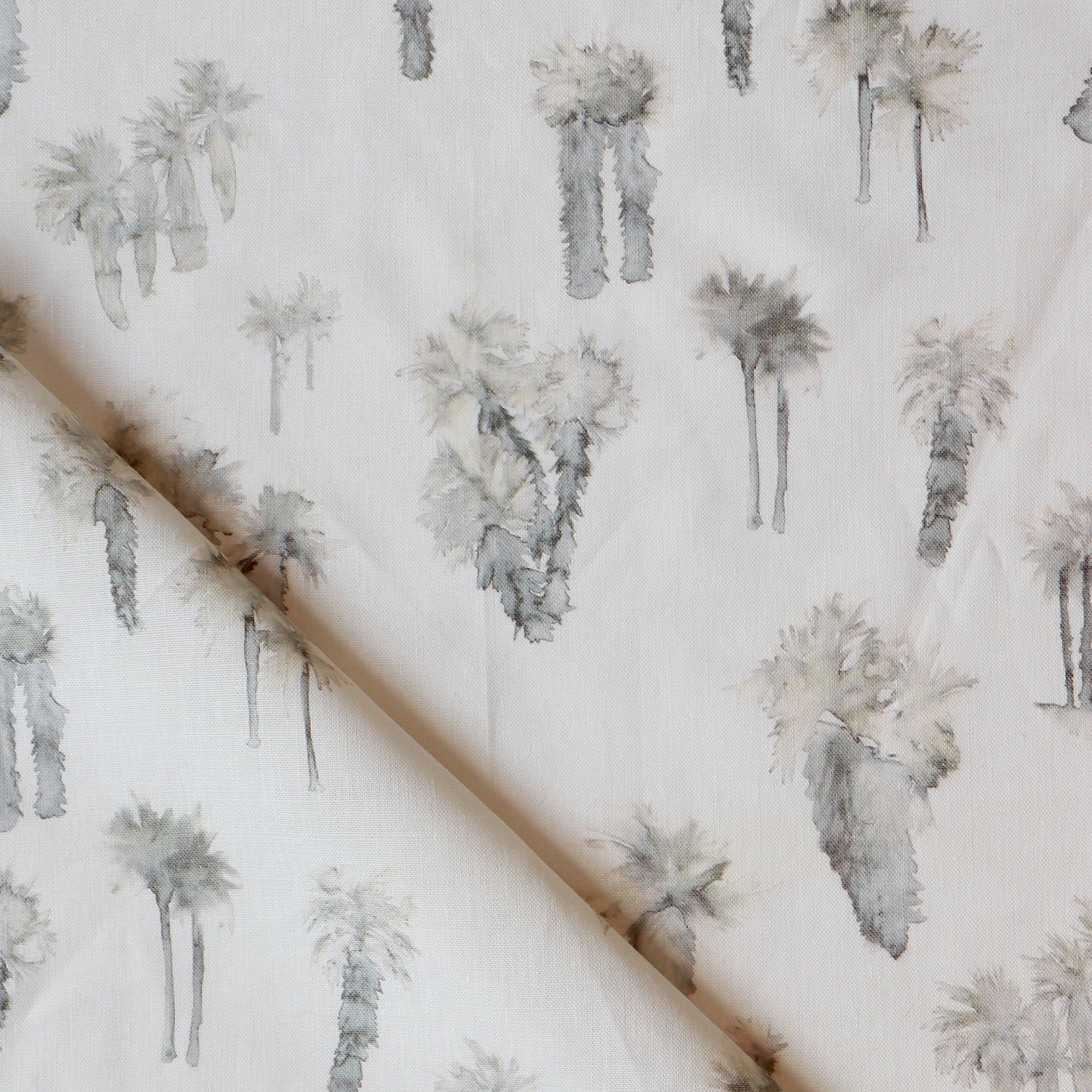 Draped fabric yardage in a painterly palm tree print in shades of gray and cream on a white field.