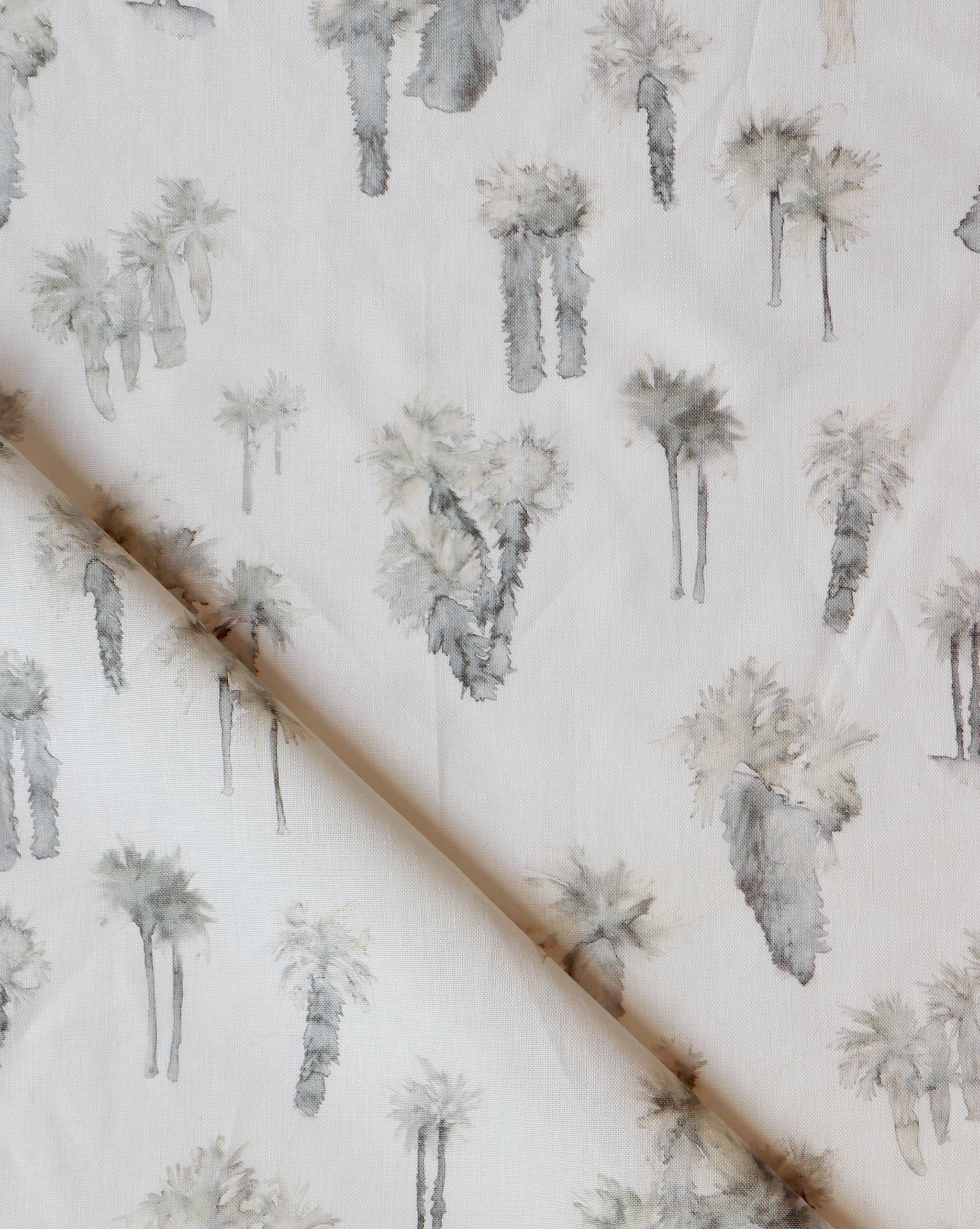 Draped fabric yardage in a painterly palm tree print in shades of gray and cream on a white field.