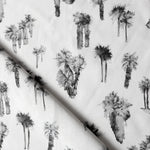 Draped fabric yardage in a painterly palm tree print in shades of gray and charcoal on a white field.