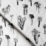 Draped fabric yardage in a painterly palm tree print in shades of gray and charcoal on a white field.