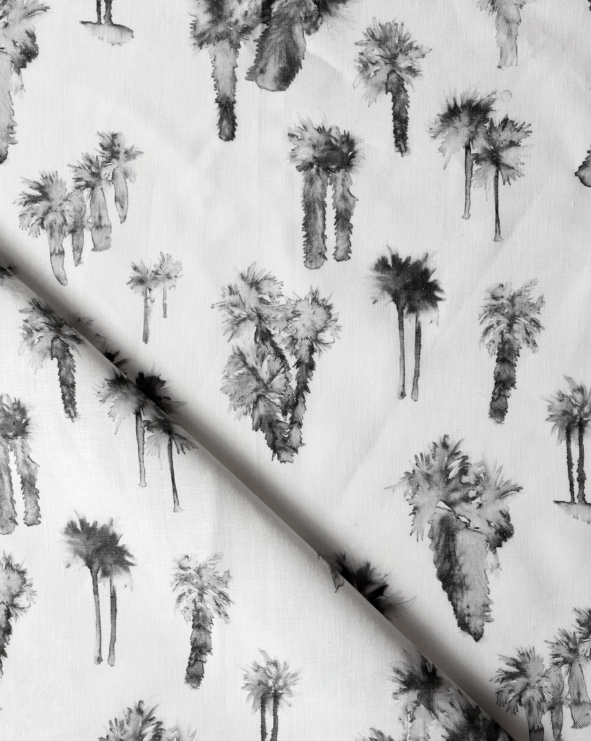 Draped fabric yardage in a painterly palm tree print in shades of gray and charcoal on a white field.