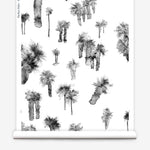 Partially unrolled wallpaper yardage in a playful palm tree print in shades of gray on a white field.