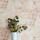 A vase of flowers stands in front of a wall covered in a playful paint blotch print in light pink on a cream field.