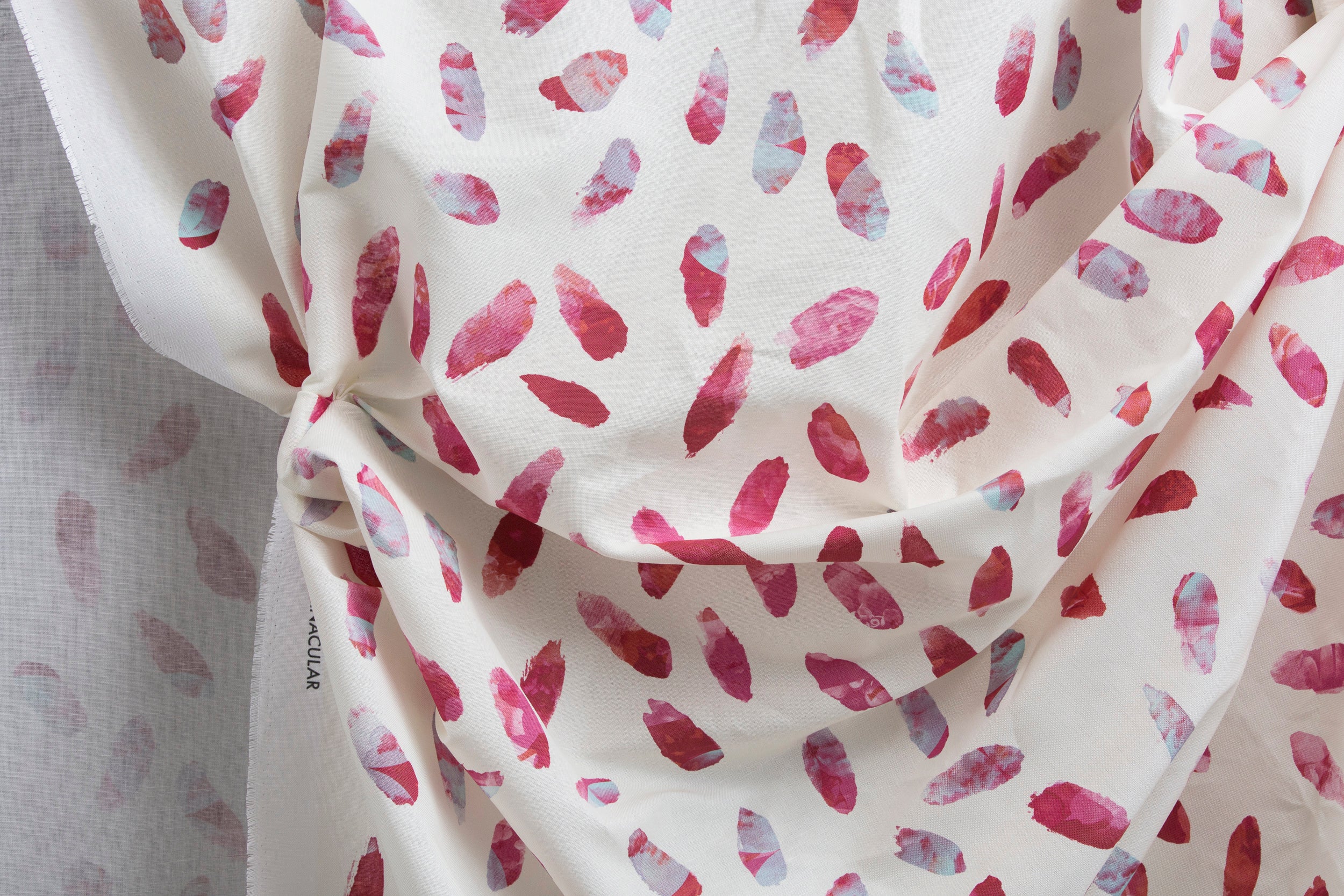 Crumpled fabric yardage in a playful paint blotch print in shades of pink and turquoise on a white field.