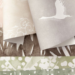 A pile of layered wallpaper swatches with delicate nature watercolor prints in shades of grey, tan, brown and green.