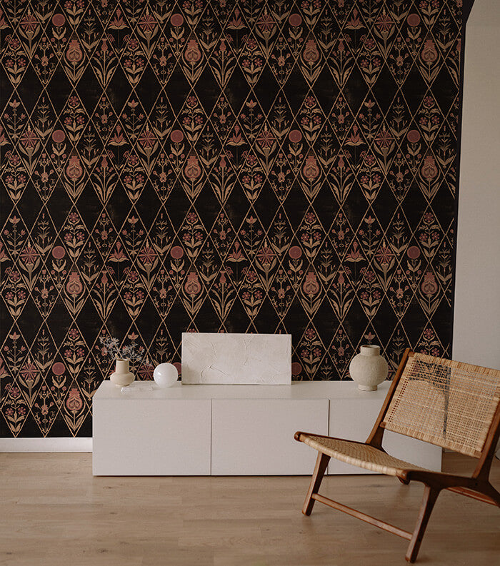 An armchair and credenza stand in front of a wall papered in a floral and diamond lattice print in pink, tan and black.