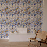 An armchair and credenza stand in front of a wall papered in a floral and diamond lattice print in blue, gold and white.