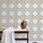 A bench with a towel and clay vases stands in front of a wall papered in a geometric lattice print in tan and white.