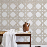 A bench with a towel and clay vases stands in front of a wall papered in a geometric lattice print in tan and white.