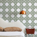 A modernist bed, hanging lamp and chair stand in front of a wall papered in a geometric lattice print in sage and white.