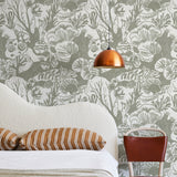 A modernist bed, hanging lamp and chair stand in front of a wall papered in a playful reef print in sage and white.