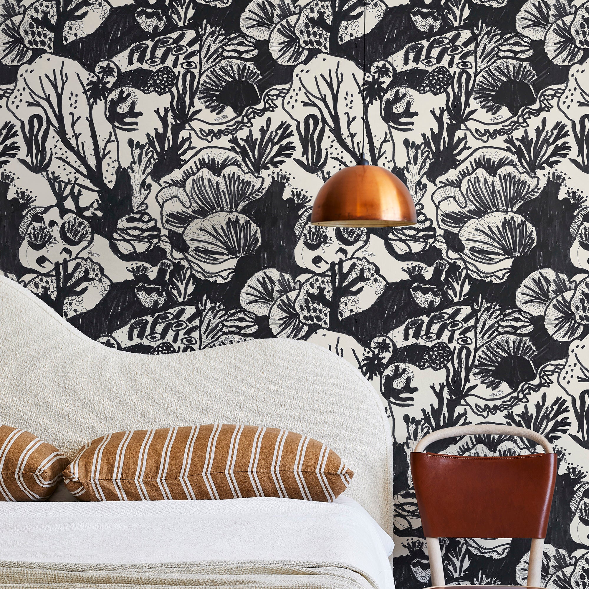 A modernist bed, hanging lamp and chair stand in front of a wall papered in a playful reef print in charcoal and white.