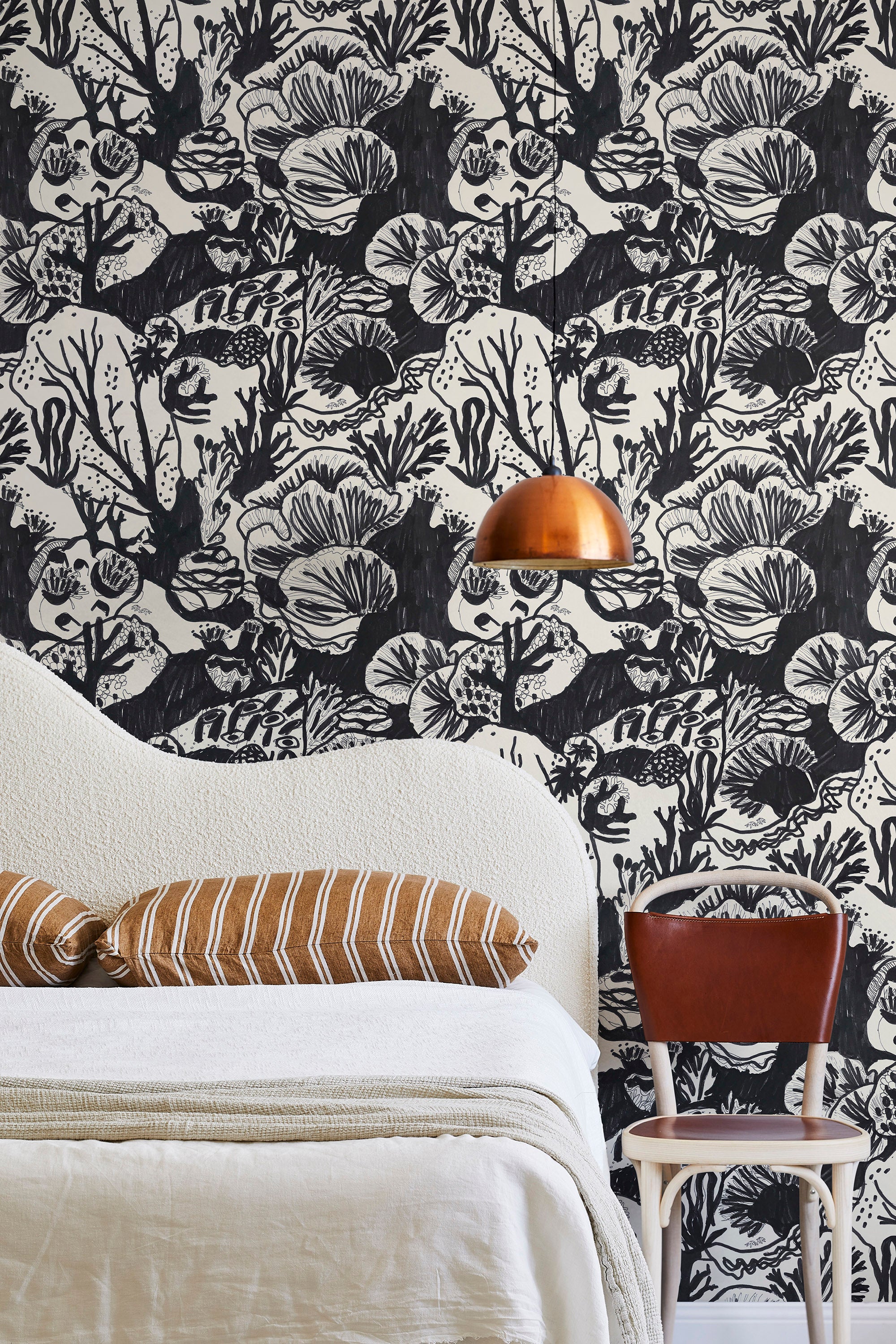 A modernist bed, hanging lamp and chair stand in front of a wall papered in a playful reef print in charcoal and white.