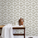 A bench with a towel and clay vases stands in front of a wall papered in a playful fish print in white and greige.