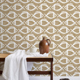 A bench with a towel and clay vases stands in front of a wall papered in a playful fish print in white and light brown.