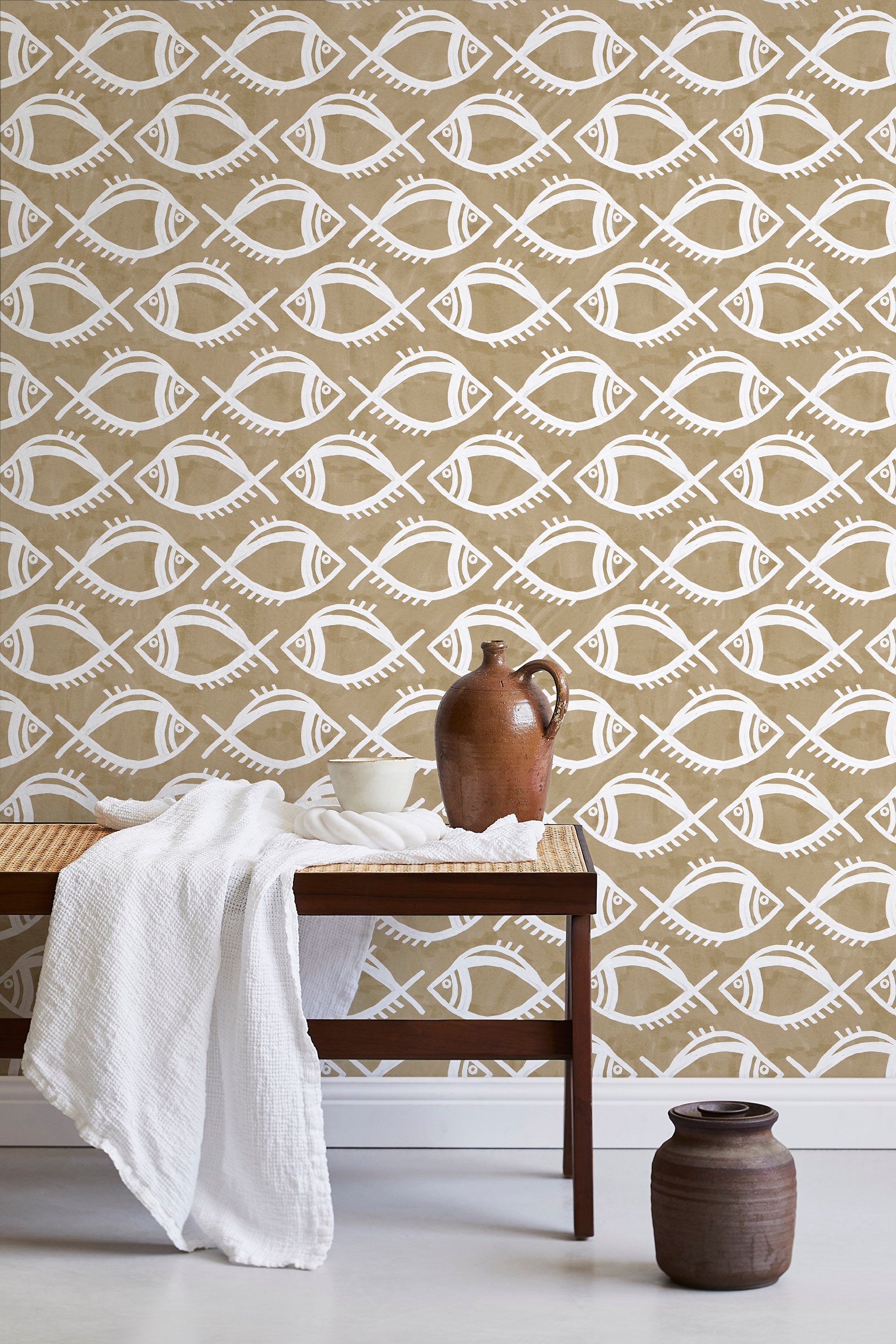 A bench with a towel and clay vases stands in front of a wall papered in a playful fish print in white and light brown.