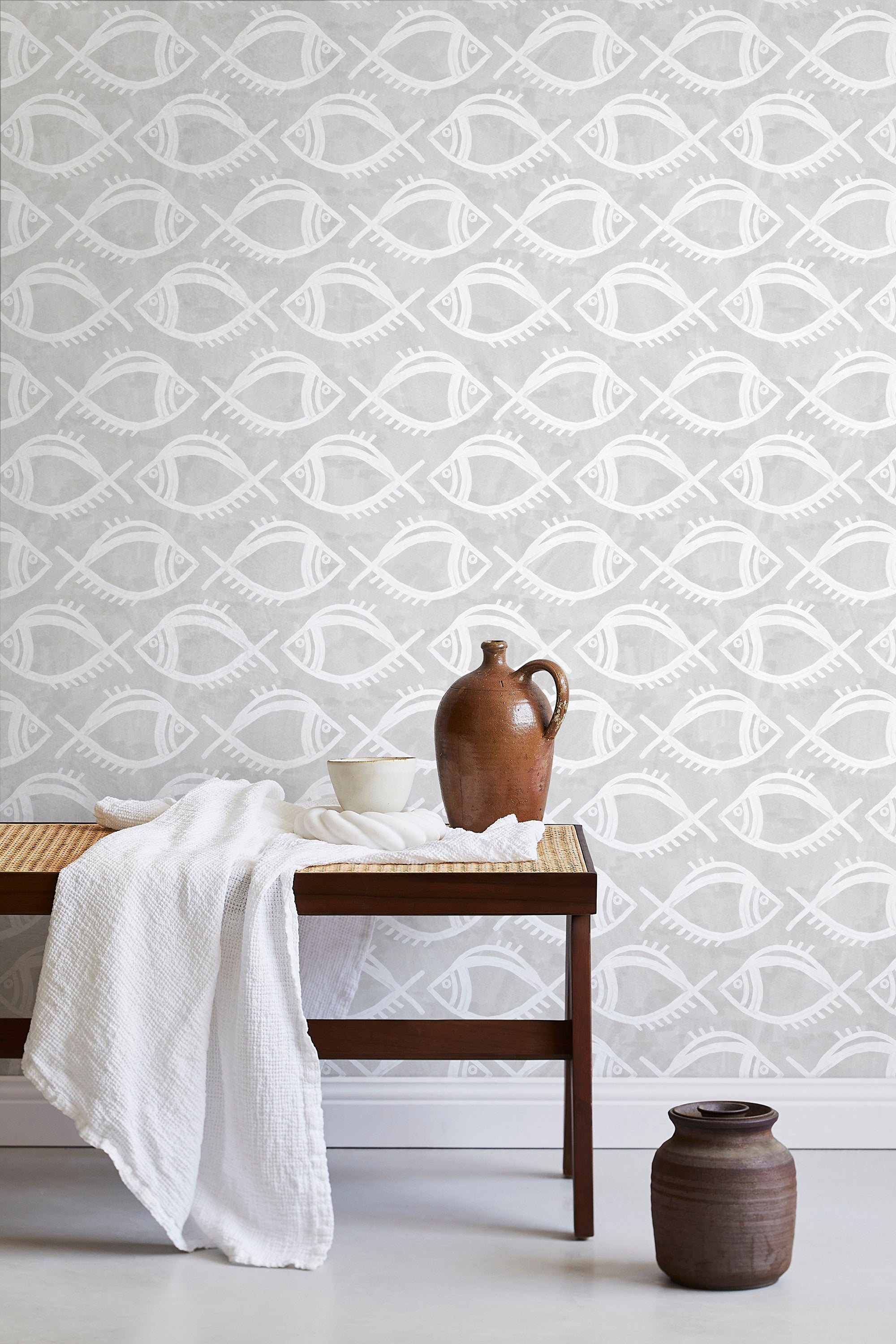 A bench with a towel and clay vases stands in front of a wall papered in a playful fish print in white and light gray.