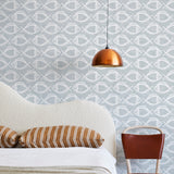 A modernist bed, hanging lamp and chair stand in front of a wall papered in a playful fish print in white and light blue.