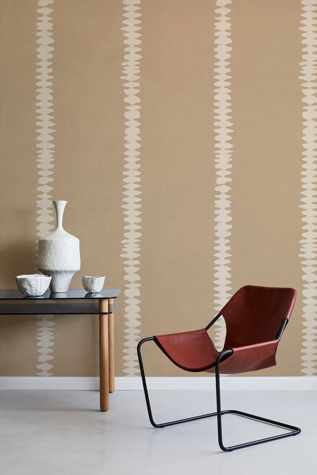 Modern interior with a red chair, table, and decorative items against a beige wall with white stripe pattern. 
