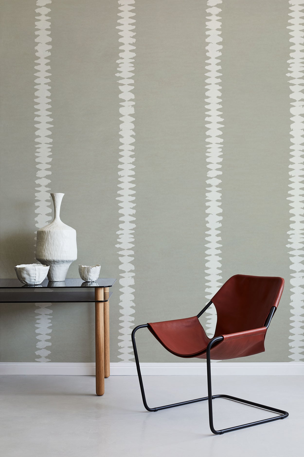 Modern interior with a red chair, table, and decorative items against a gray wall with white stripe pattern.