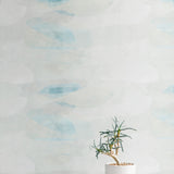 A potted plant stands in front of a wall covered in an abstract color blot print in shades of white, gray and turquoise.