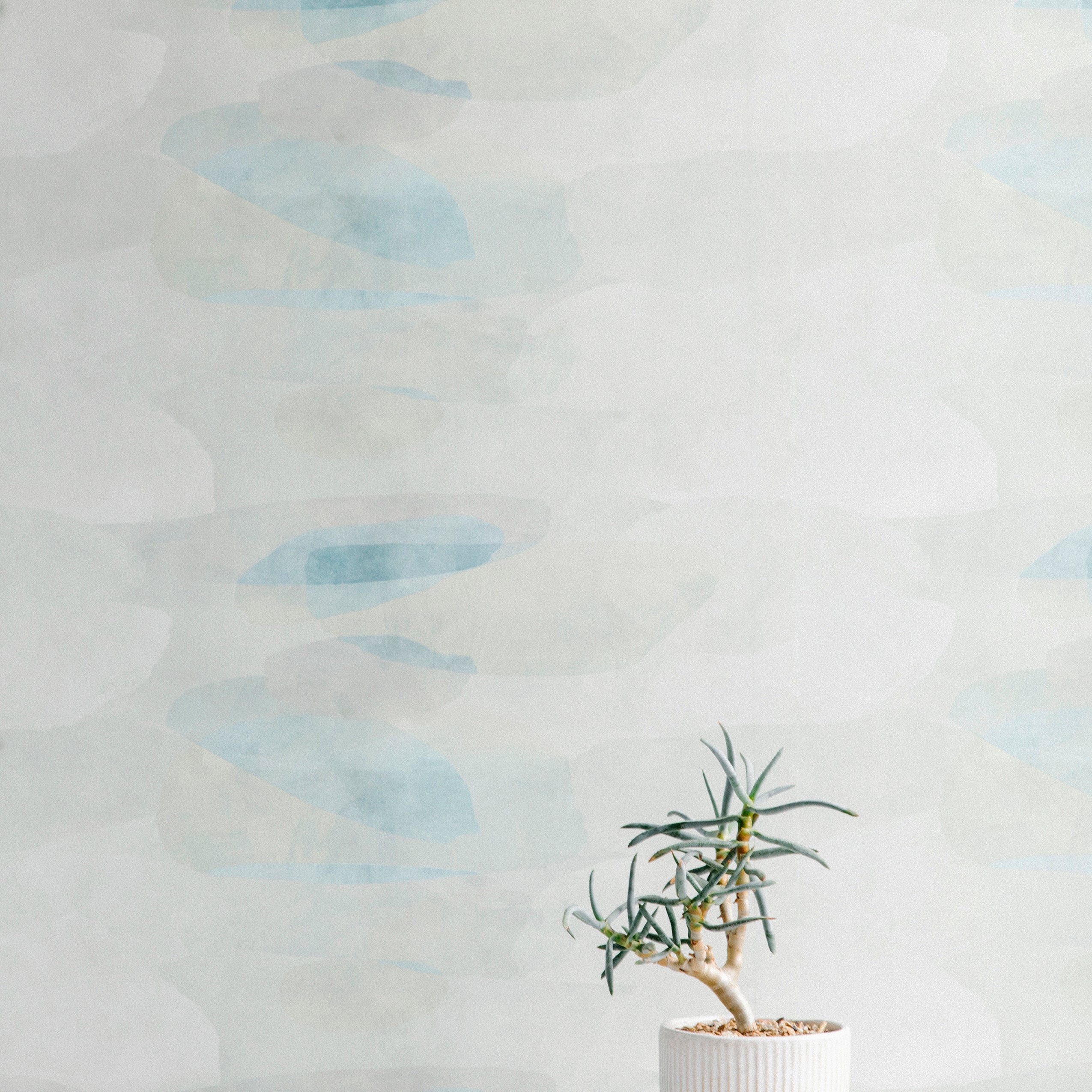 A potted plant stands in front of a wall covered in an abstract color blot print in shades of white, gray and turquoise.