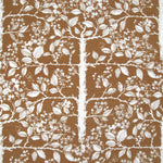 Detail of fabric in a large-scale tree and leaf print in cream on a brown field.