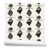 Partially unrolledwallpaper in a large-scale pattern of black watercolored diamonds, circles and lines on a cream background. 