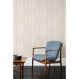 A wooden chair and coffee table in front of a wall papered in a striped print inspired by Japanese shibori on a washed beige background.