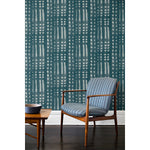 A wooden chair and coffee table in front of a wall papered in a striped print inspired by Japanese shibori on a washed denim background.