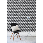 A chair and floor lamp in front of a wall papered in a hand-painted tumbling block pattern in black and gray on a white background.