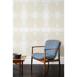 A wooden chair and coffee table in front of a wall papered in a dense hand-drawn symmetrical pattern in shades of beige on a white background.