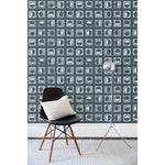 A chair and floor lamp in front of a wall papered in rows of block-printed white moons in various phases on a charcoal background.