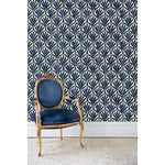 An antique chair in front of a wall papered in a repeating Moroccan-inspired scallop pattern in navy and green on a white background.