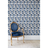 An antique chair in front of a wall papered in a repeating pattern of large-scale graphic flowers in shades of blue on a cream background.