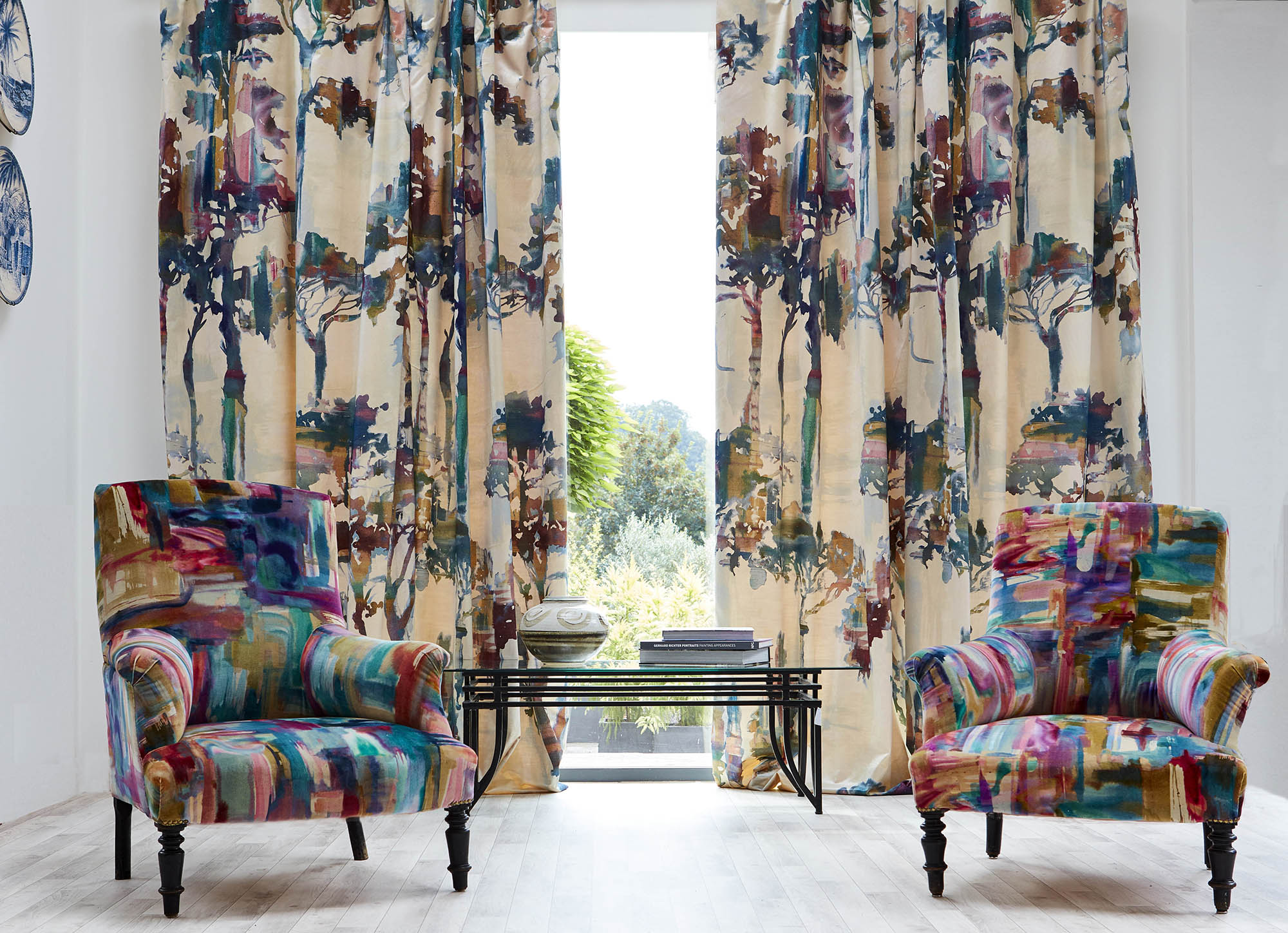 A living space with colorful armchairs and curtains upholstered in a painterly tree print.