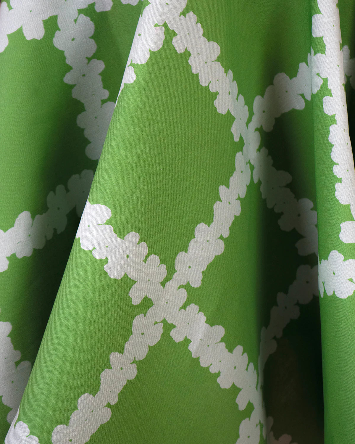 Draped fabric yardage in a floral grid print in white on a green field.