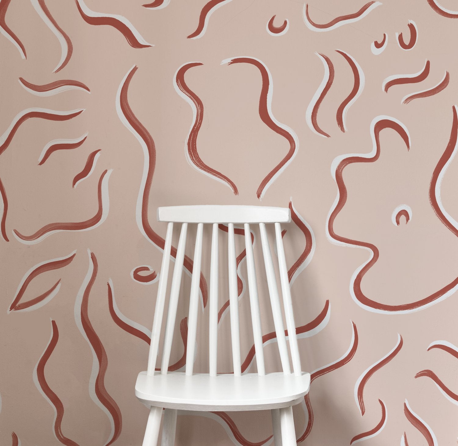 A wooden chair stands in front of a wall papered in a painterly botanical print in rust and white on a light pink field.