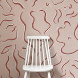 A wooden chair stands in front of a wall papered in a painterly botanical print in rust and white on a light pink field.