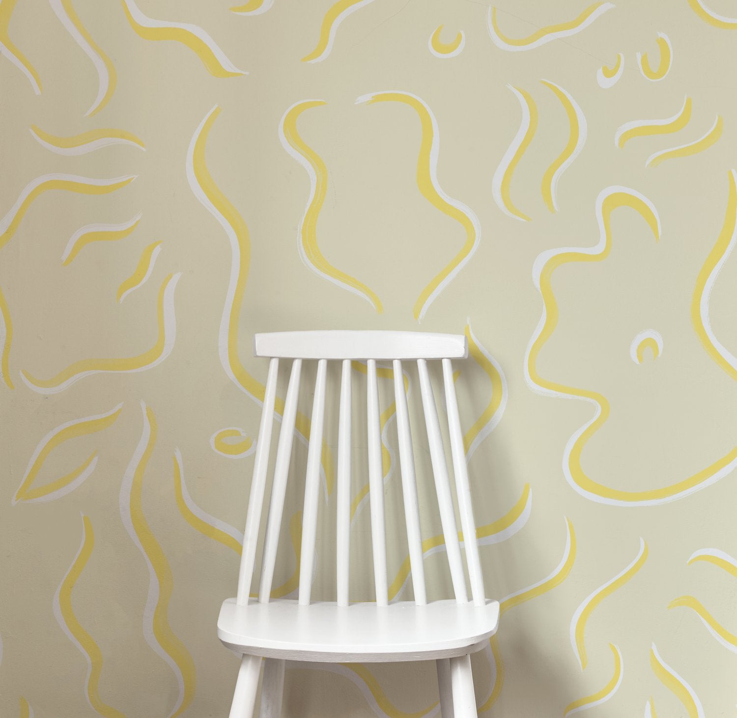 A wooden chair stands in front of a wall papered in a painterly botanical print in yellow and white on a tan field.